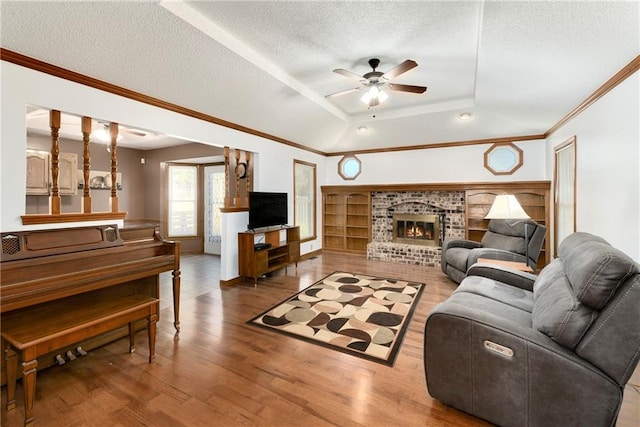 living room with ornamental molding, a brick fireplace, a textured ceiling, light hardwood / wood-style floors, and ceiling fan