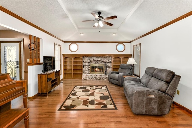 living room featuring hardwood / wood-style flooring, a brick fireplace, a raised ceiling, a textured ceiling, and ceiling fan