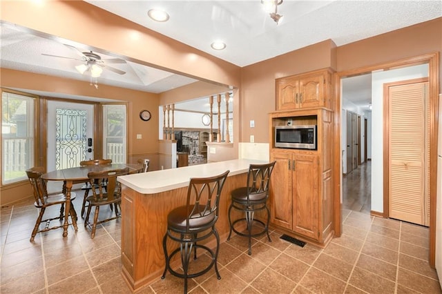 kitchen featuring a kitchen breakfast bar, kitchen peninsula, light tile patterned floors, and ceiling fan