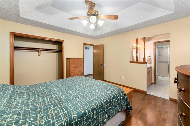 bedroom featuring a raised ceiling, ceiling fan, dark hardwood / wood-style flooring, a closet, and ensuite bath