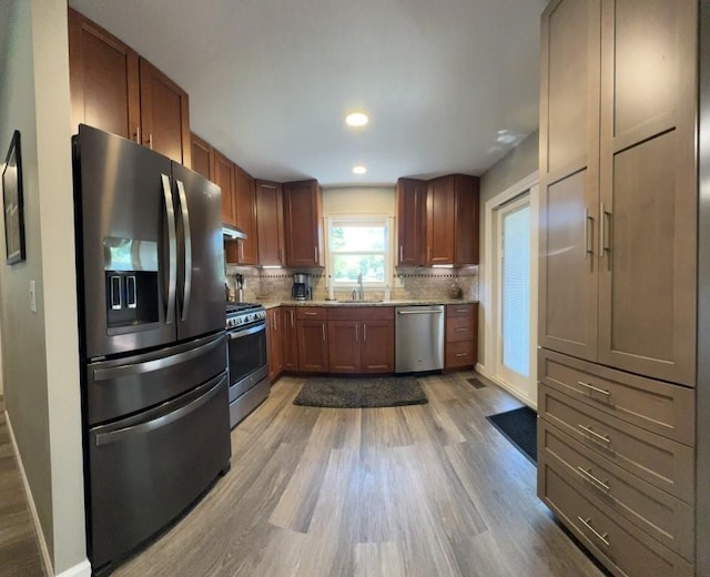 kitchen with stainless steel appliances, sink, tasteful backsplash, and light hardwood / wood-style flooring