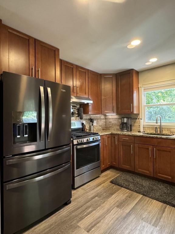 kitchen featuring light stone countertops, sink, light hardwood / wood-style floors, appliances with stainless steel finishes, and backsplash