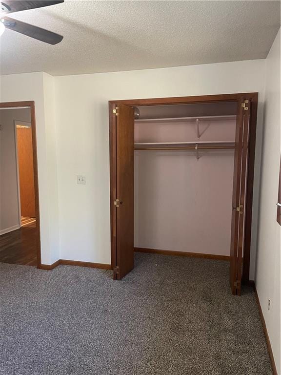 unfurnished bedroom with dark colored carpet, ceiling fan, a closet, and a textured ceiling