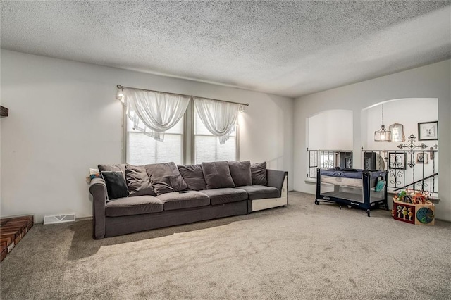 living room with a notable chandelier, a textured ceiling, carpet flooring, and a healthy amount of sunlight