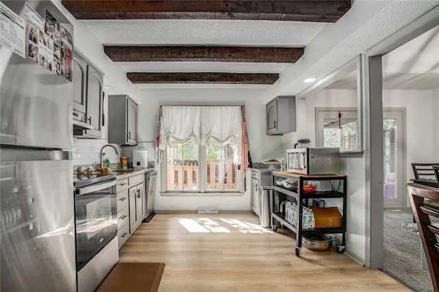 kitchen featuring gray cabinets, appliances with stainless steel finishes, beamed ceiling, and a healthy amount of sunlight