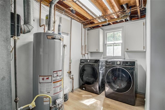 washroom featuring water heater, washing machine and clothes dryer, light hardwood / wood-style floors, and cabinets