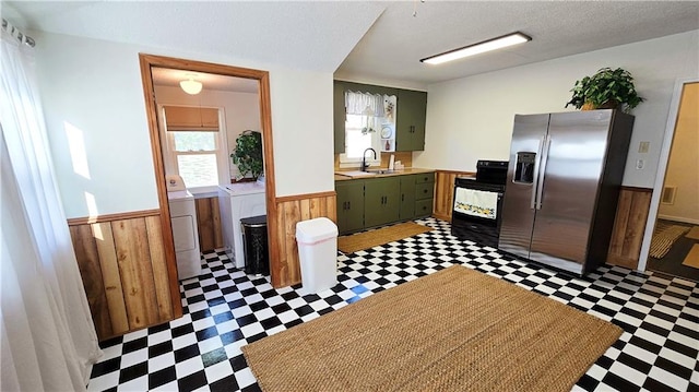 kitchen featuring washing machine and clothes dryer, electric range, green cabinets, sink, and stainless steel fridge with ice dispenser