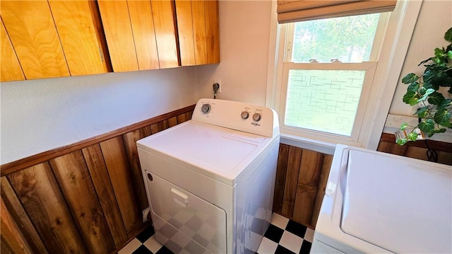 clothes washing area featuring wooden walls, separate washer and dryer, and cabinets