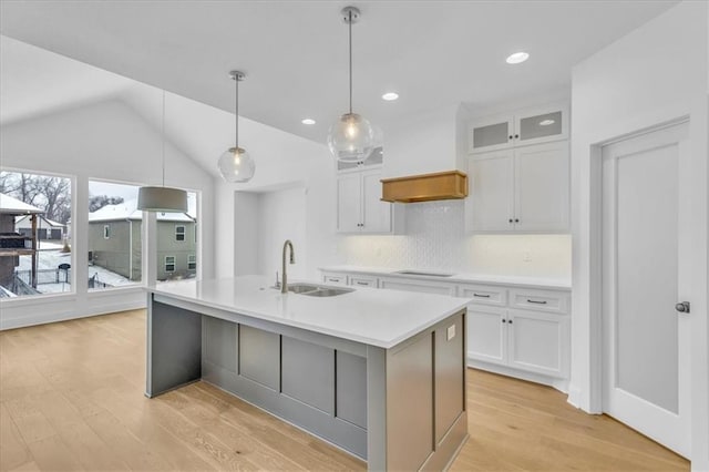 kitchen with a kitchen island with sink, custom range hood, a sink, white cabinetry, and cooktop