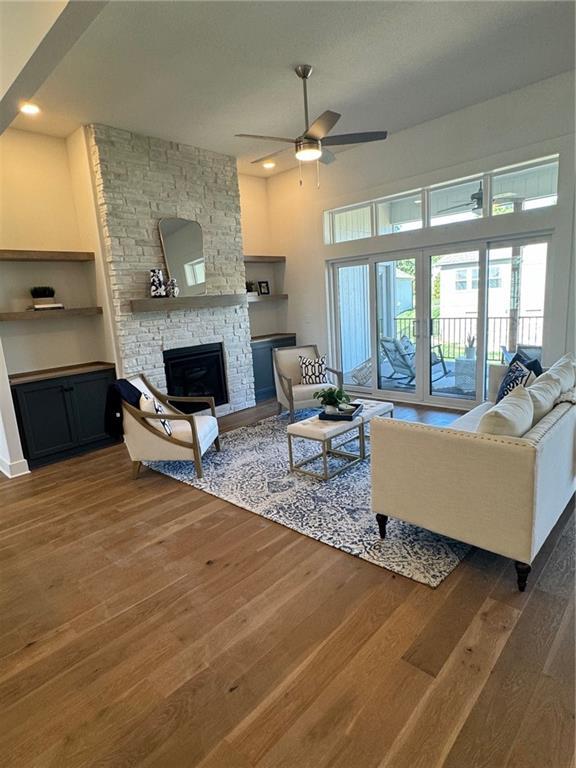 living area with a stone fireplace, a ceiling fan, and wood finished floors