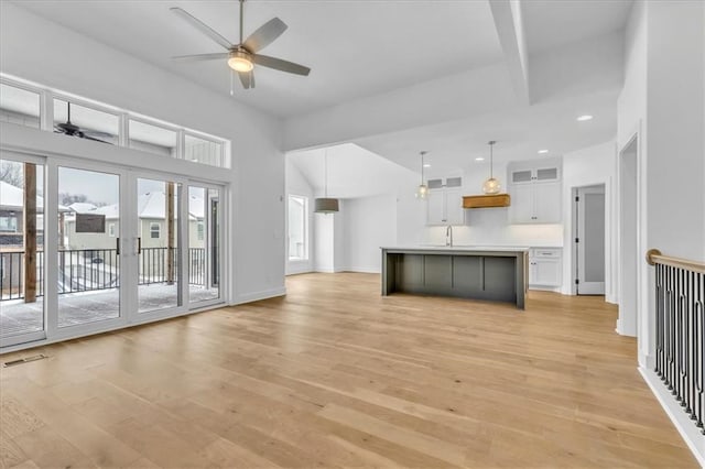 unfurnished living room with baseboards, visible vents, a sink, ceiling fan, and light wood-style floors