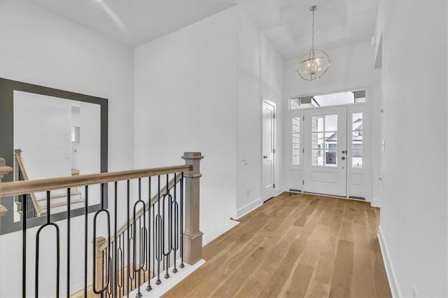 entryway featuring wood finished floors, baseboards, a towering ceiling, and a chandelier