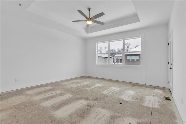 empty room featuring a tray ceiling, a ceiling fan, baseboards, and visible vents