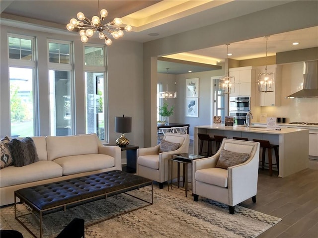 living room featuring hardwood / wood-style flooring, sink, a tray ceiling, and an inviting chandelier