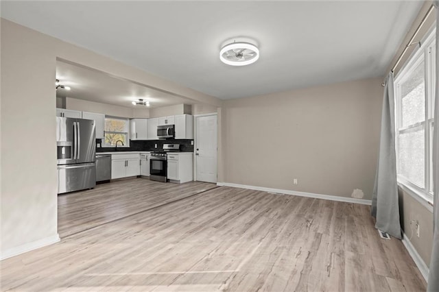 kitchen with decorative backsplash, sink, white cabinets, light wood-type flooring, and appliances with stainless steel finishes