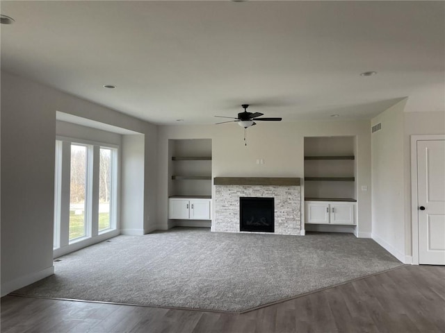 unfurnished living room featuring a stone fireplace, wood-type flooring, ceiling fan, and built in features