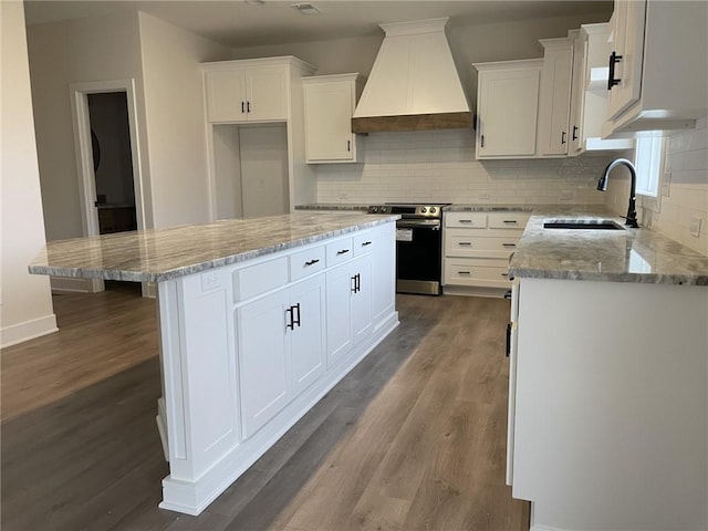 kitchen with wood-type flooring, a center island, white cabinetry, stainless steel electric stove, and premium range hood