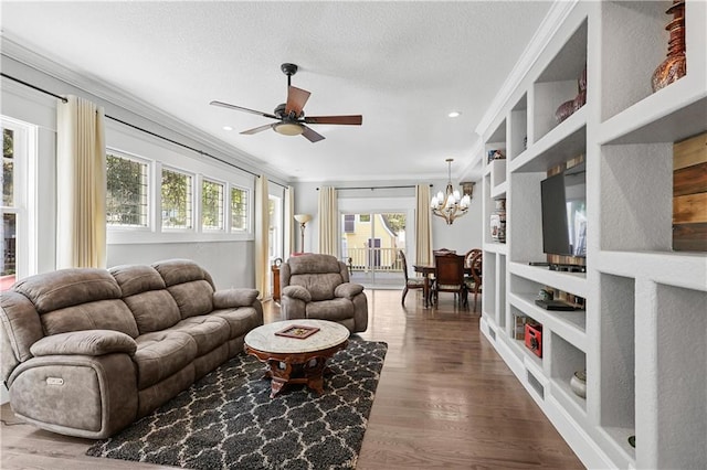 living room with wood-type flooring, ceiling fan with notable chandelier, ornamental molding, built in shelves, and a textured ceiling