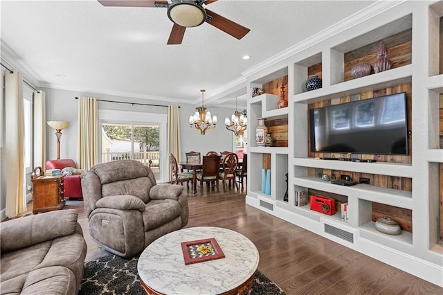 living room featuring built in shelves, ornamental molding, ceiling fan with notable chandelier, and dark hardwood / wood-style flooring