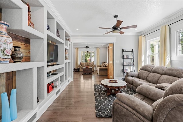 living room featuring ceiling fan, wood-type flooring, ornamental molding, built in shelves, and a textured ceiling