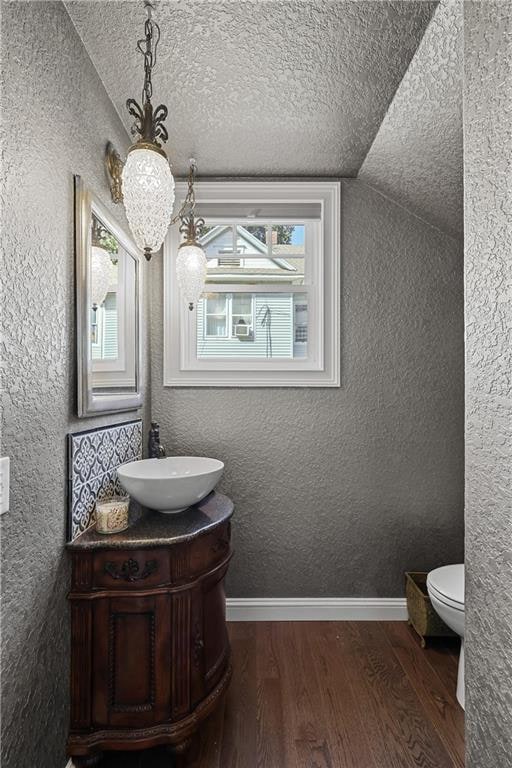 bathroom featuring lofted ceiling, hardwood / wood-style floors, vanity, toilet, and a textured ceiling