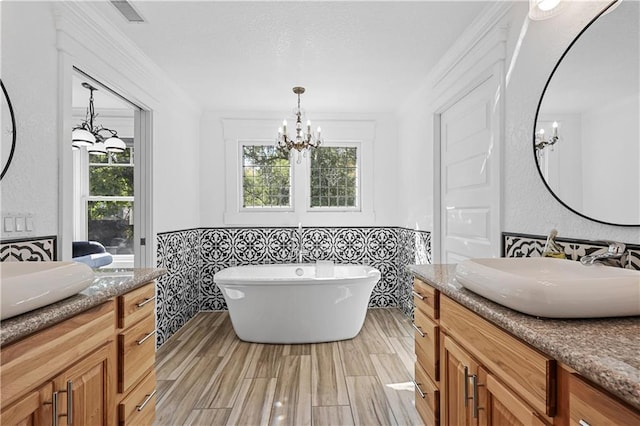 bathroom with an inviting chandelier, a tub, vanity, and tile walls