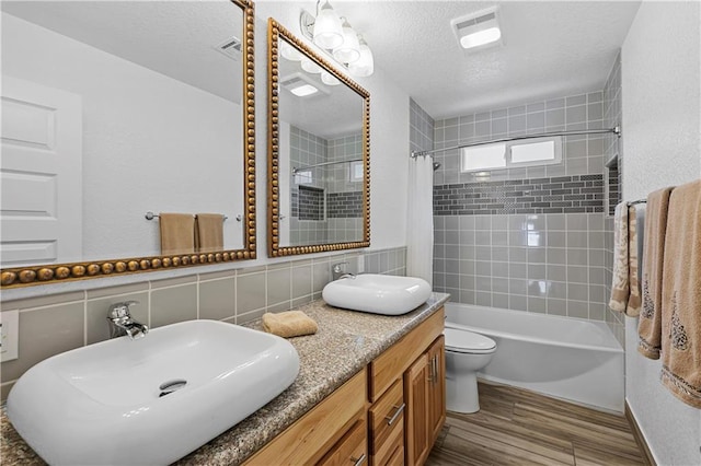 full bathroom with shower / tub combo with curtain, hardwood / wood-style floors, vanity, toilet, and a textured ceiling