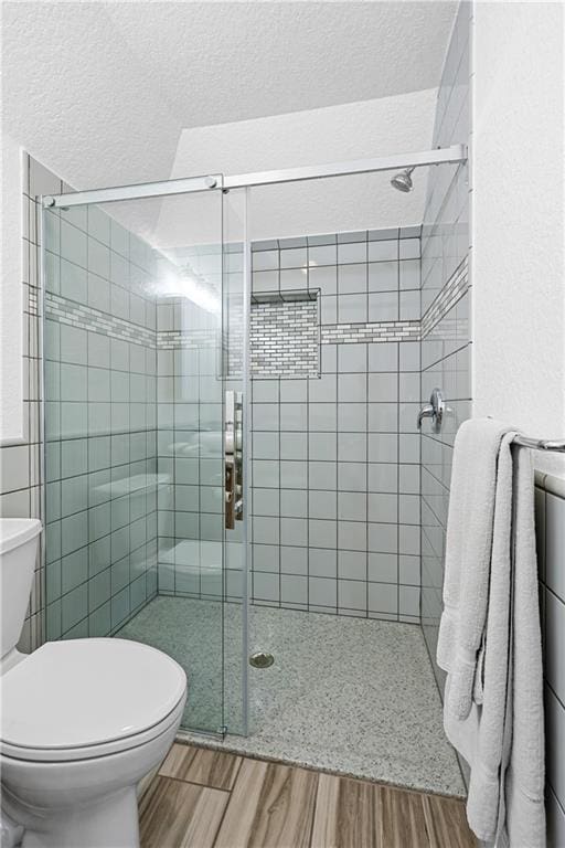 bathroom with wood-type flooring, a shower with shower door, a textured ceiling, and toilet