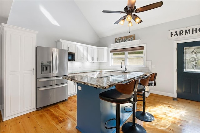 kitchen featuring stainless steel fridge, white cabinetry, light hardwood / wood-style floors, dark stone counters, and a breakfast bar area