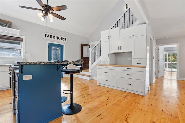 kitchen featuring a breakfast bar area, high vaulted ceiling, light wood-style flooring, ceiling fan, and white cabinets