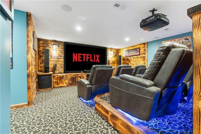 carpeted home theater with visible vents, baseboards, and wooden walls