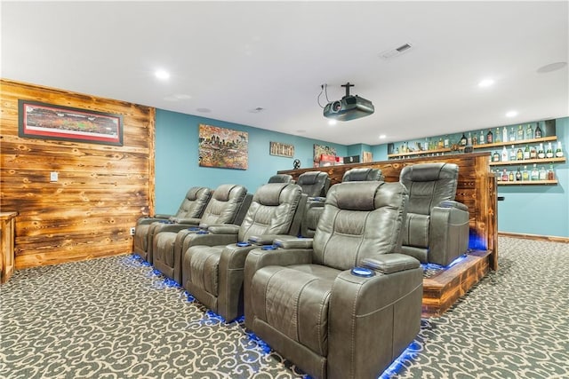 carpeted home theater room featuring visible vents, recessed lighting, a bar, and wooden walls