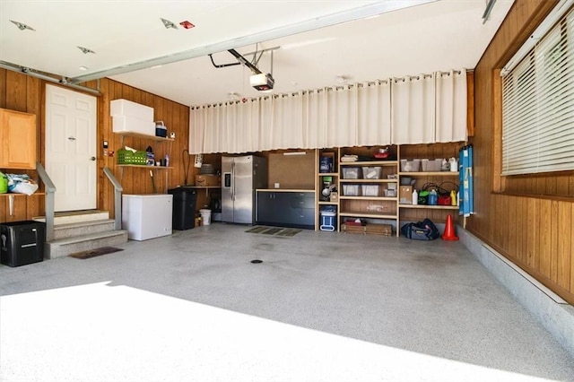 garage featuring stainless steel fridge with ice dispenser, a garage door opener, and wooden walls