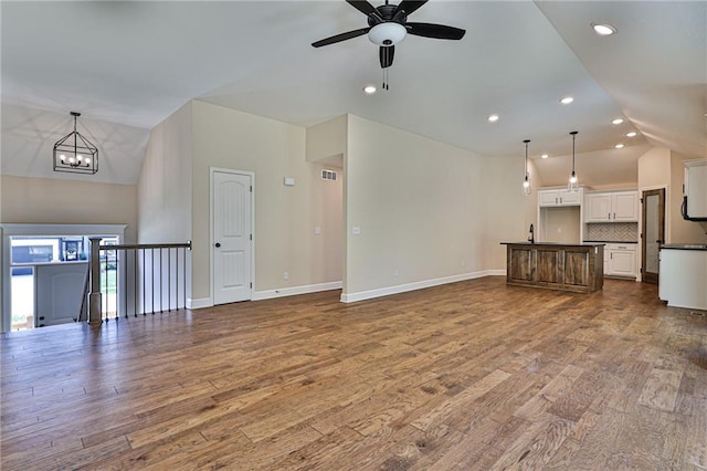 unfurnished living room featuring vaulted ceiling, sink, ceiling fan with notable chandelier, and hardwood / wood-style floors