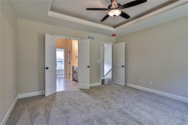 unfurnished bedroom with a raised ceiling, ceiling fan, light colored carpet, and ornamental molding