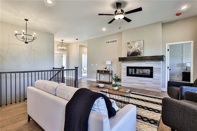 living room with ceiling fan with notable chandelier, a fireplace, and hardwood / wood-style floors