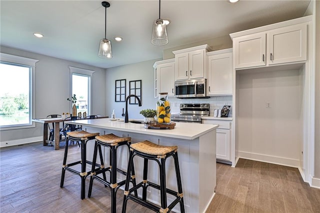 kitchen with white cabinets, a center island with sink, appliances with stainless steel finishes, and pendant lighting