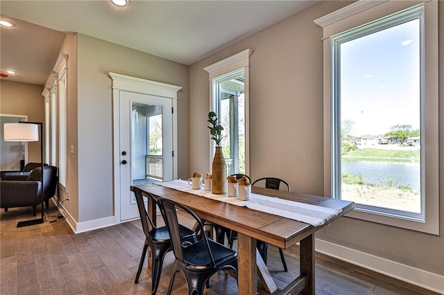 dining space with a water view, dark wood-type flooring, and plenty of natural light