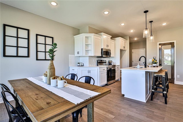 kitchen featuring wood-type flooring, white cabinetry, stainless steel appliances, and decorative light fixtures