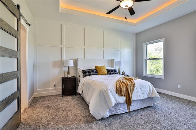 bedroom featuring ceiling fan, a raised ceiling, a barn door, and carpet