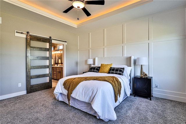 carpeted bedroom with ceiling fan, a tray ceiling, ensuite bath, and a barn door