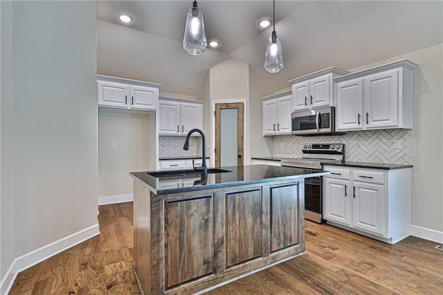 kitchen with appliances with stainless steel finishes, vaulted ceiling, hardwood / wood-style floors, and an island with sink