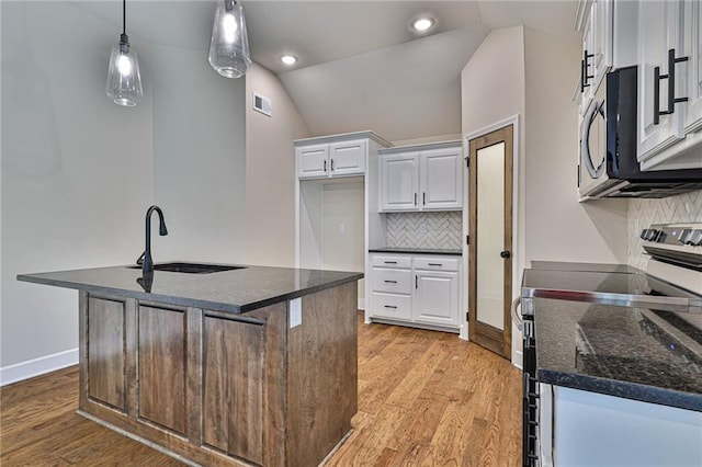 kitchen featuring light hardwood / wood-style floors, a kitchen island with sink, white cabinetry, appliances with stainless steel finishes, and decorative light fixtures