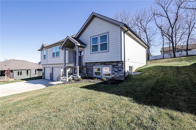 raised ranch with a front yard, stone siding, concrete driveway, and a garage
