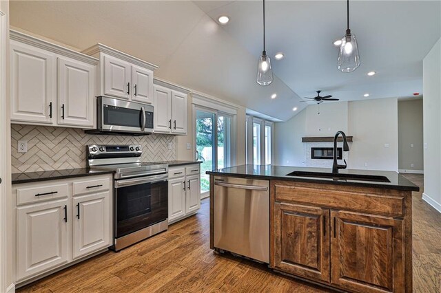 kitchen with vaulted ceiling, dark countertops, a sink, and stainless steel appliances