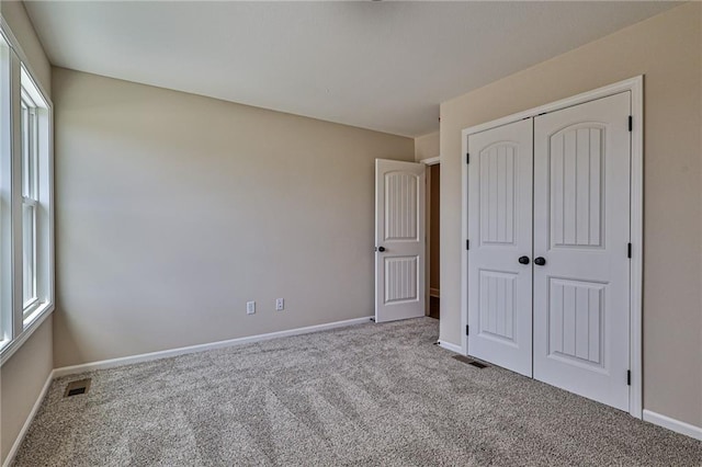 unfurnished bedroom featuring a closet, visible vents, multiple windows, and carpet