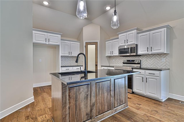 kitchen featuring stainless steel appliances, vaulted ceiling, a center island with sink, and light hardwood / wood-style floors