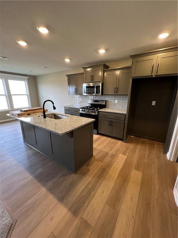 kitchen featuring a center island with sink, sink, light wood-type flooring, light stone countertops, and appliances with stainless steel finishes