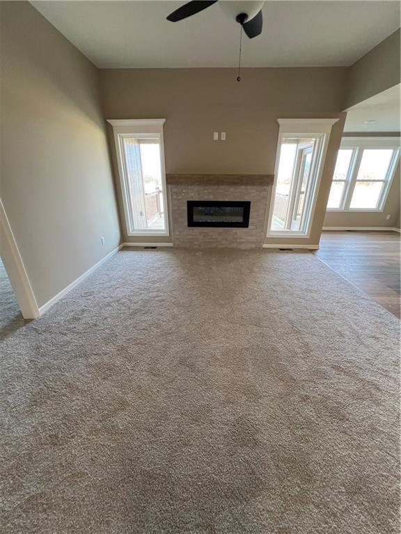 unfurnished living room featuring carpet flooring, a wealth of natural light, and ceiling fan