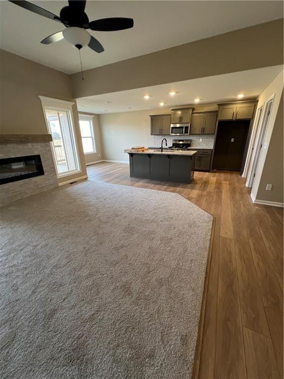 kitchen with decorative backsplash, ceiling fan, sink, a center island with sink, and hardwood / wood-style flooring